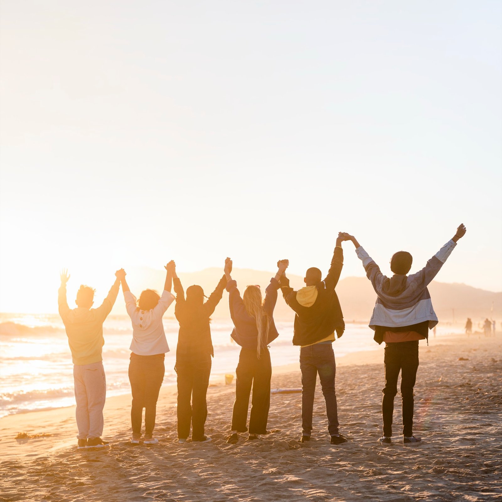 People holding hands on a beach at sunrise